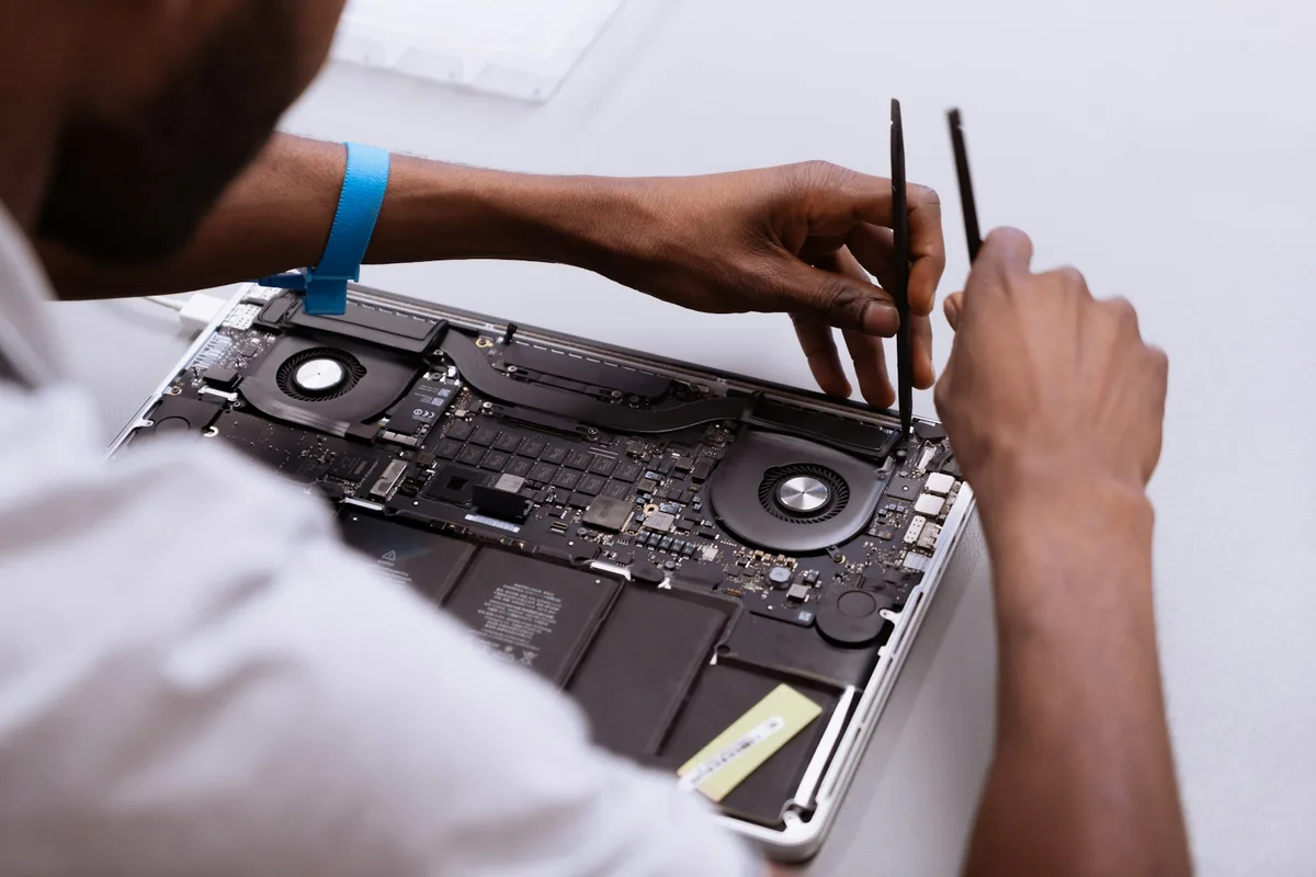 Manos de un técnico trabajando con herramientas de precisión dentro de una laptop abierta